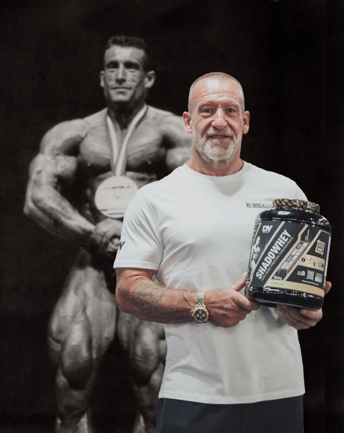 Dorian Yates today holding DY Shadowhey Concentrate, in front of a photo from his Mr. Olympia years